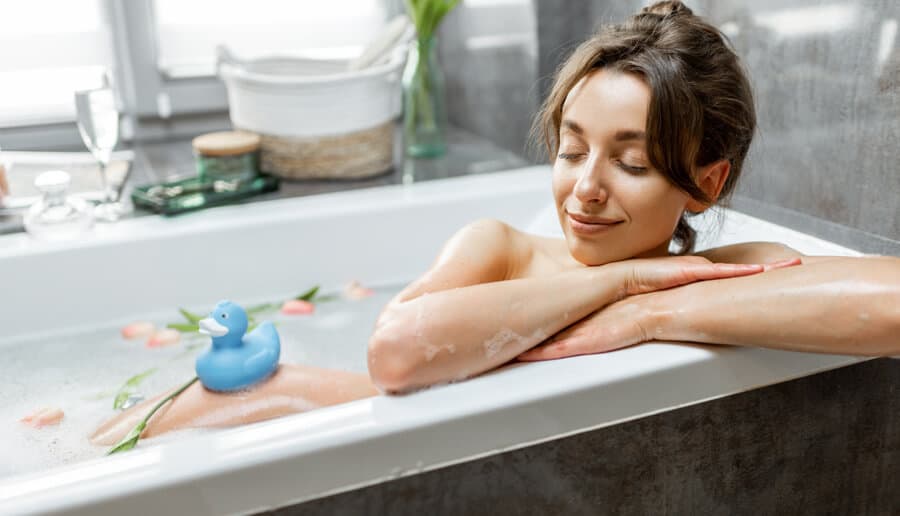 mulher tomando banho em banheira ao lado de patinho de borracha azul.