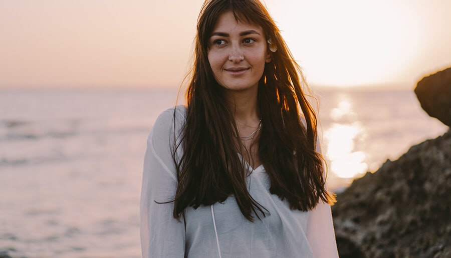 Mulher com saída de praia e mar no fundo.